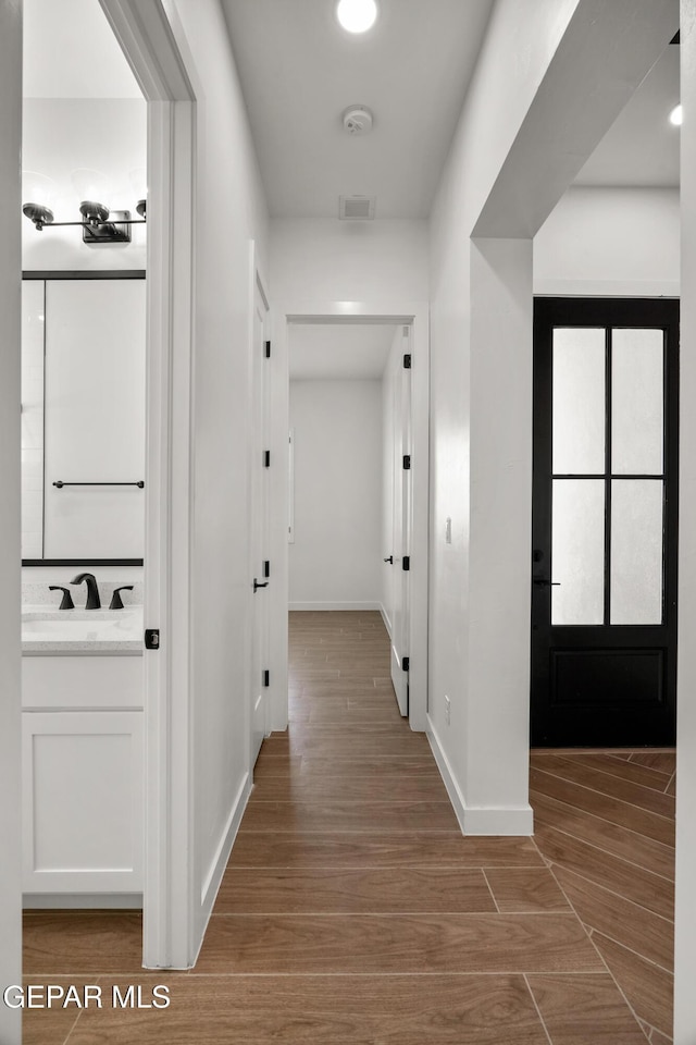 hall featuring baseboards, wood finished floors, visible vents, and a sink