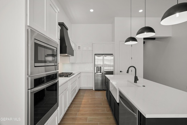 kitchen featuring wood finish floors, light countertops, appliances with stainless steel finishes, wall chimney exhaust hood, and a sink