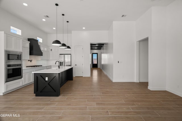 kitchen featuring wood finish floors, white cabinetry, stainless steel appliances, wall chimney exhaust hood, and light countertops