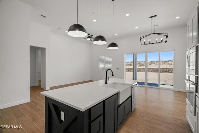 kitchen with a sink, light countertops, light wood-style floors, appliances with stainless steel finishes, and ceiling fan with notable chandelier