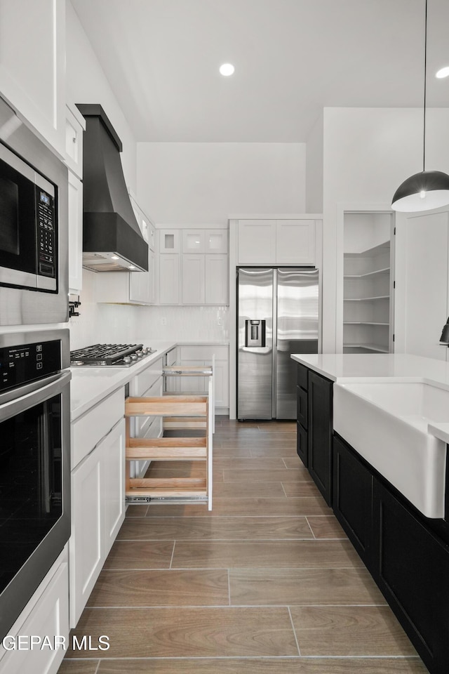 kitchen featuring wood finish floors, a sink, wall chimney range hood, stainless steel appliances, and light countertops