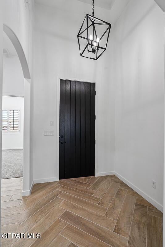 entryway featuring baseboards, arched walkways, and a chandelier