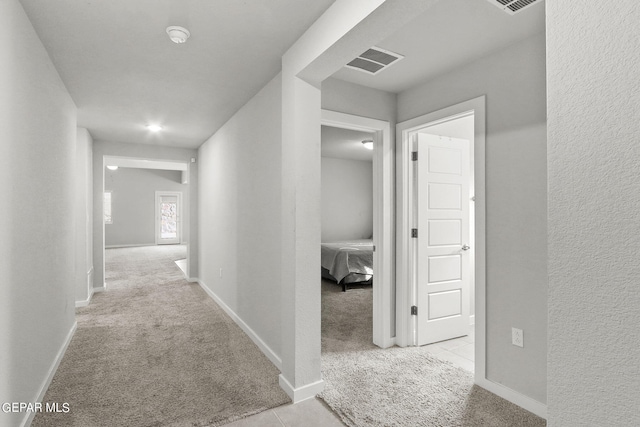 hall featuring light colored carpet, visible vents, and baseboards