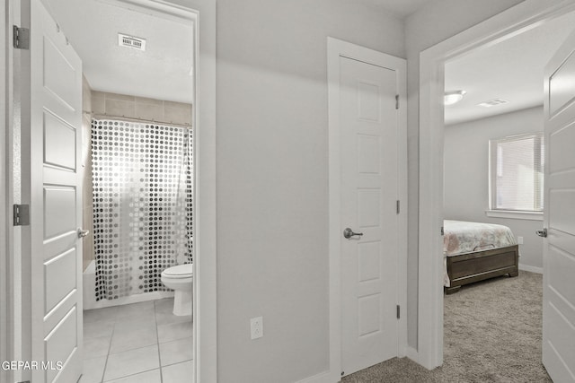 ensuite bathroom featuring tile patterned flooring, visible vents, toilet, and baseboards