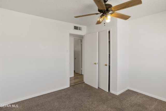 unfurnished room with visible vents, dark carpet, a textured ceiling, and a ceiling fan