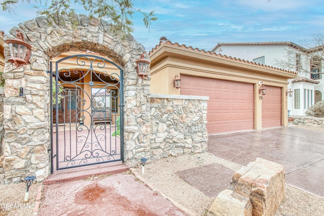 view of exterior entry with stucco siding, a gate, stone siding, concrete driveway, and a garage