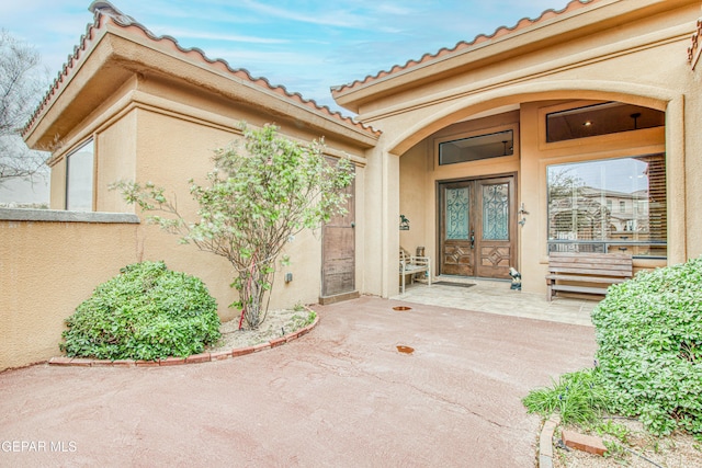 view of exterior entry with stucco siding, french doors, and a patio