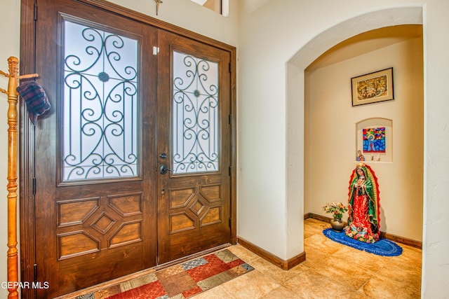 foyer entrance with arched walkways and baseboards