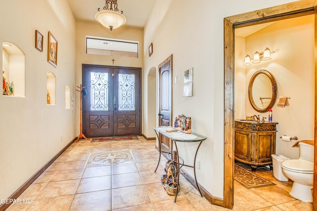 foyer featuring arched walkways, light tile patterned floors, french doors, and baseboards