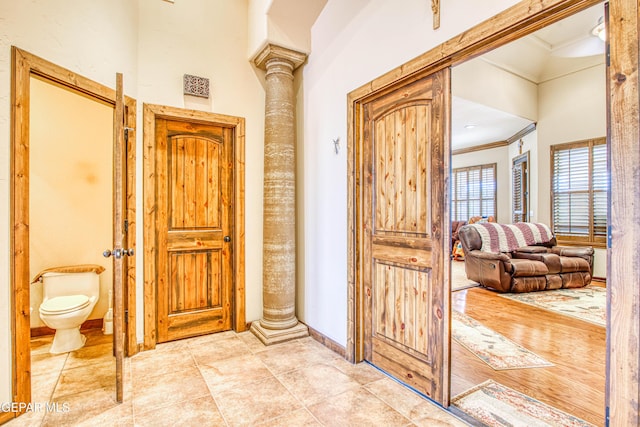 hall featuring tile patterned floors, decorative columns, baseboards, and crown molding