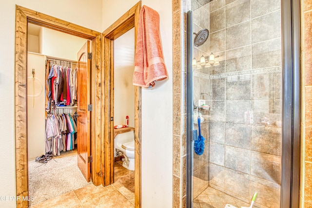 bathroom featuring tile patterned flooring, a spacious closet, toilet, and a stall shower