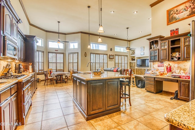 kitchen featuring a center island with sink, stainless steel microwave, a breakfast bar area, light tile patterned floors, and ceiling fan