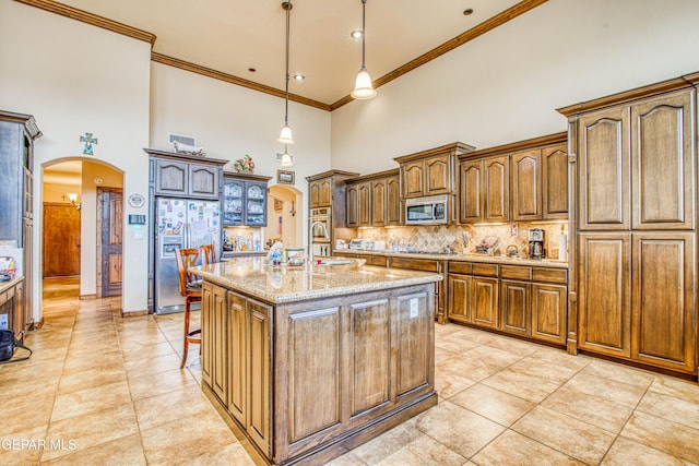 kitchen featuring light stone counters, arched walkways, stainless steel appliances, decorative backsplash, and a towering ceiling