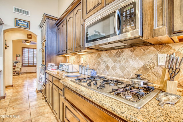 kitchen featuring visible vents, backsplash, light stone countertops, arched walkways, and stainless steel appliances