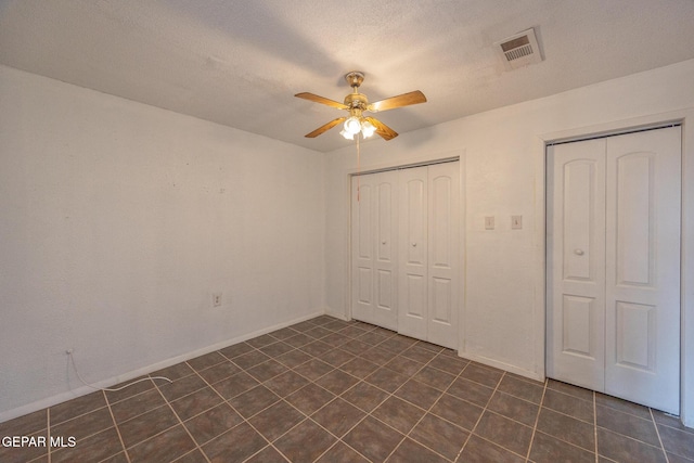 unfurnished bedroom featuring a ceiling fan, baseboards, visible vents, dark tile patterned flooring, and a textured ceiling