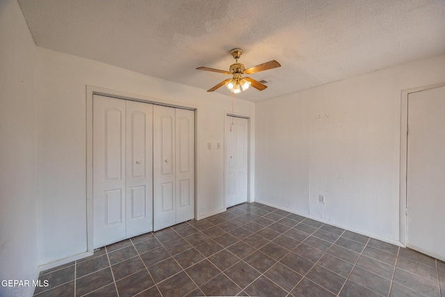 unfurnished bedroom with a closet, dark tile patterned floors, a textured ceiling, and ceiling fan