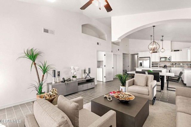 living area with visible vents, baseboards, ceiling fan with notable chandelier, arched walkways, and high vaulted ceiling