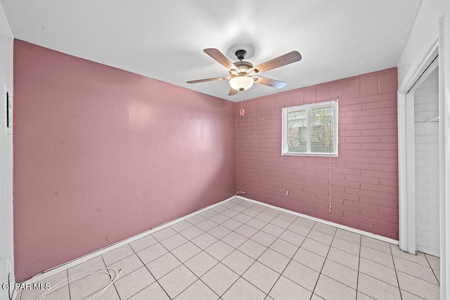 empty room with ceiling fan, brick wall, and light tile patterned flooring