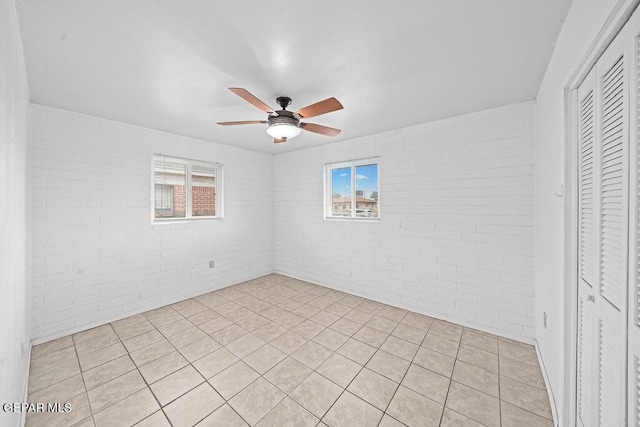 unfurnished room featuring ceiling fan and brick wall