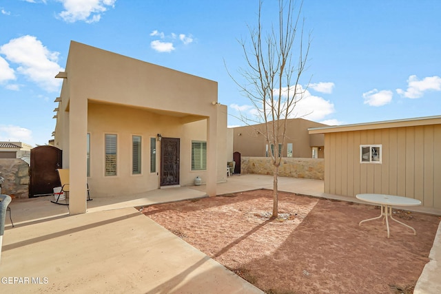 rear view of house with stucco siding, a patio, and fence