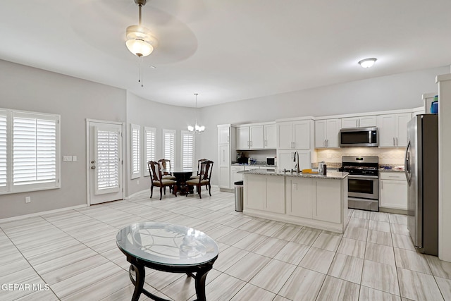 kitchen featuring tasteful backsplash, light stone counters, ceiling fan with notable chandelier, stainless steel appliances, and a sink