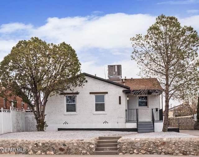 view of front of house featuring brick siding, central AC, and fence