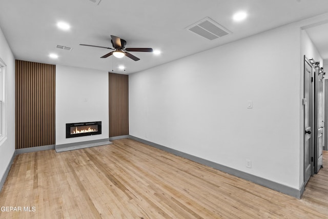 unfurnished living room with visible vents, light wood-style floors, a glass covered fireplace, and a ceiling fan