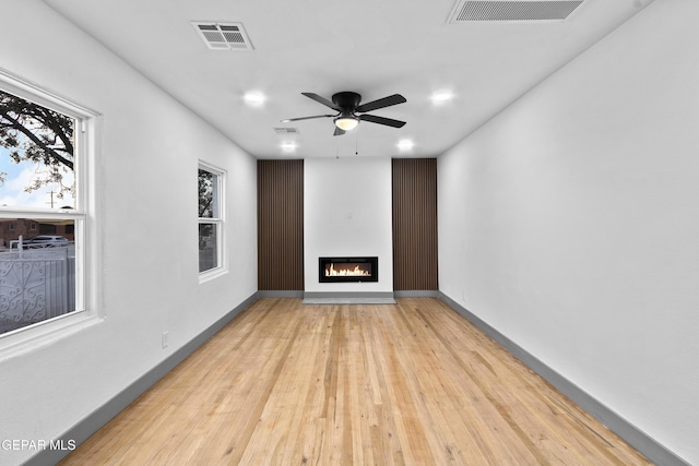 unfurnished living room with visible vents, baseboards, ceiling fan, and a glass covered fireplace