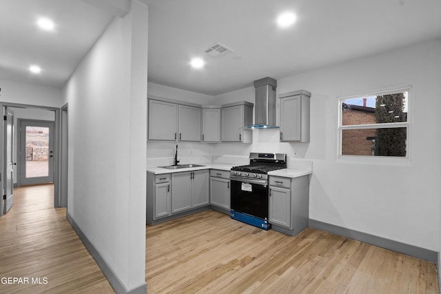 kitchen with visible vents, gray cabinets, a sink, gas stove, and wall chimney range hood