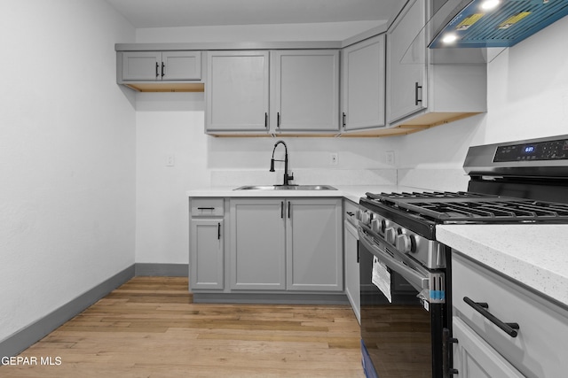 kitchen featuring light wood-type flooring, stainless steel gas stove, gray cabinets, a sink, and wall chimney range hood