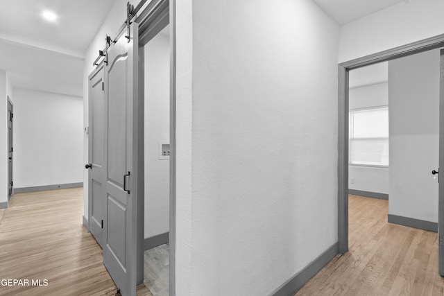 hallway with light wood-type flooring, a barn door, and baseboards