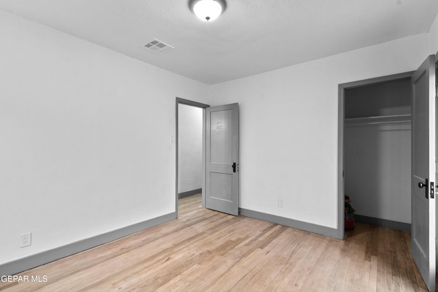 unfurnished bedroom with light wood-style flooring, baseboards, visible vents, and a closet