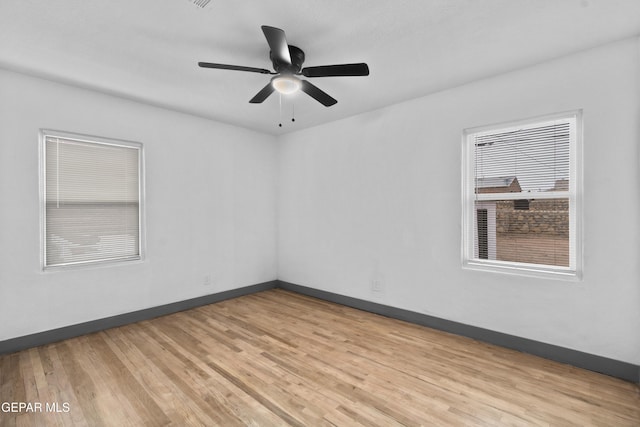 spare room with light wood finished floors, a ceiling fan, and baseboards