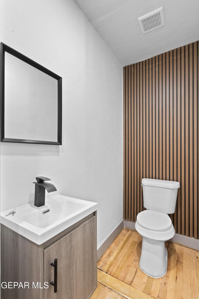 half bathroom with visible vents, baseboards, toilet, wood finished floors, and vanity