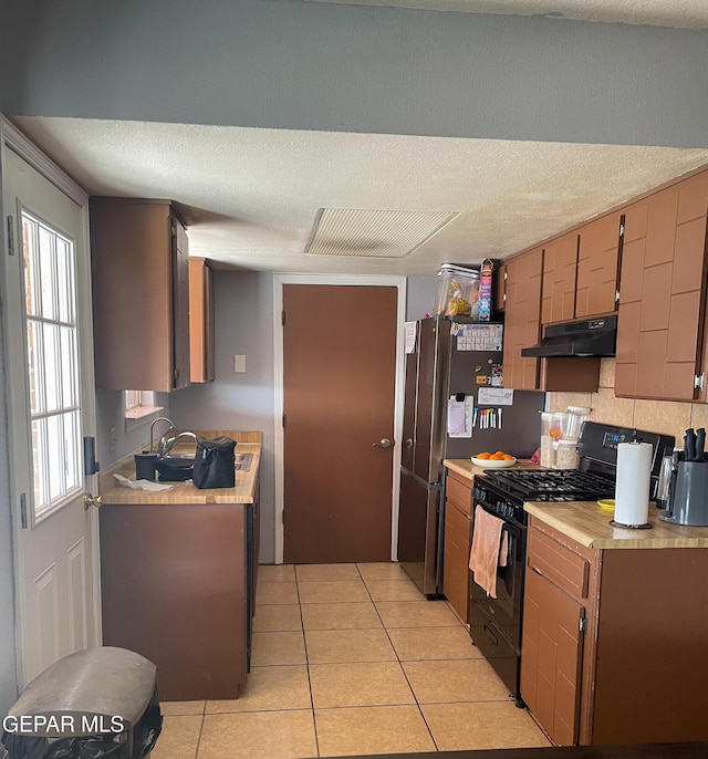 kitchen featuring black range with gas cooktop, light countertops, under cabinet range hood, and light tile patterned flooring