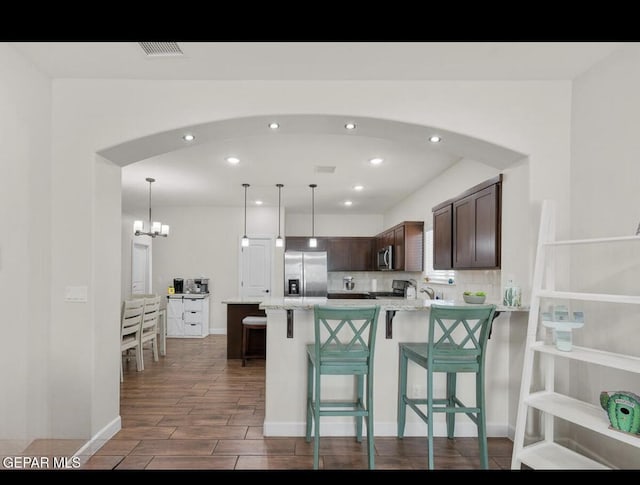 kitchen featuring a kitchen breakfast bar, arched walkways, dark brown cabinetry, appliances with stainless steel finishes, and a peninsula