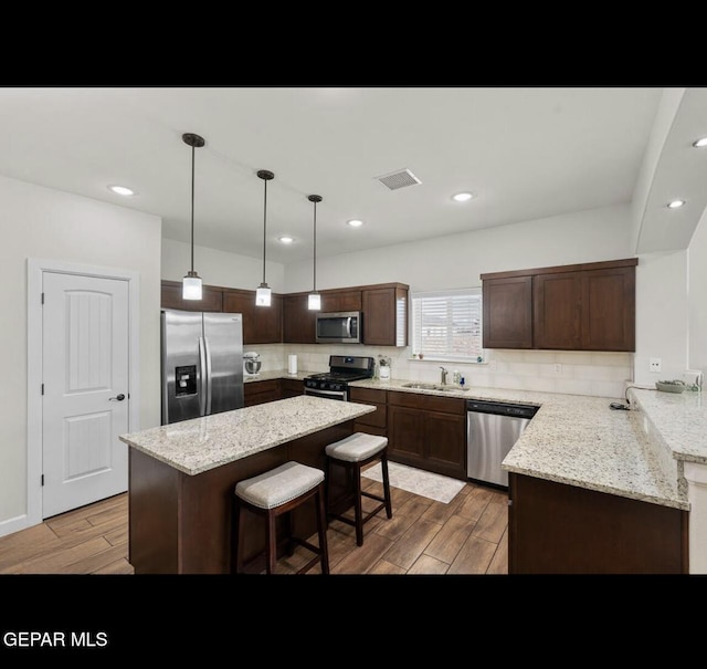 kitchen featuring visible vents, a breakfast bar, a sink, appliances with stainless steel finishes, and light wood finished floors