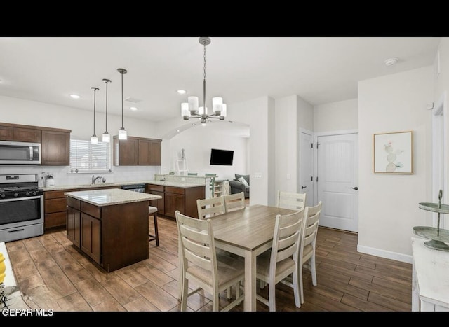 kitchen featuring wood finished floors, a center island, appliances with stainless steel finishes, an inviting chandelier, and decorative backsplash