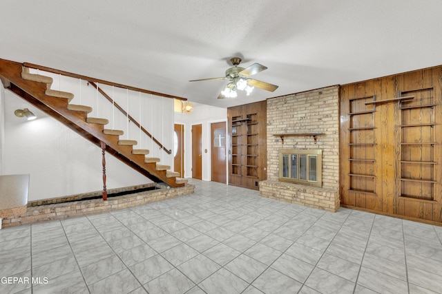 unfurnished living room featuring stairway, built in shelves, a fireplace, ceiling fan, and a textured ceiling