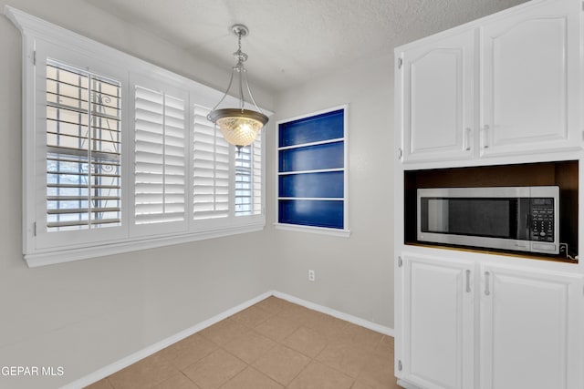 unfurnished dining area featuring light tile patterned flooring, a textured ceiling, and baseboards