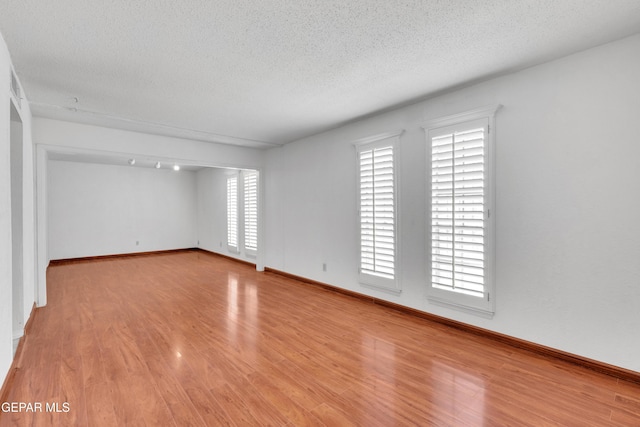 unfurnished room with light wood-style flooring, baseboards, and a textured ceiling