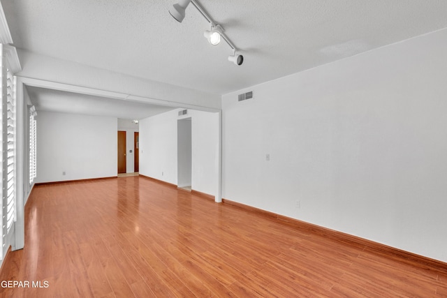 empty room with visible vents, baseboards, a textured ceiling, and light wood finished floors