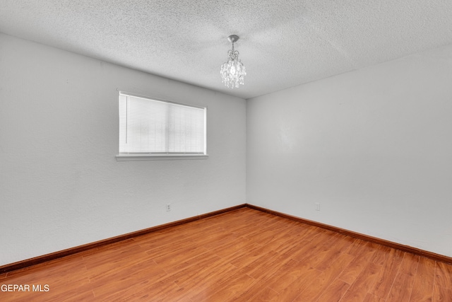 spare room with a notable chandelier, baseboards, light wood-type flooring, and a textured ceiling
