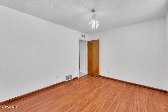 empty room with a chandelier, visible vents, light wood finished floors, and a textured ceiling