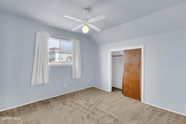 unfurnished bedroom featuring a ceiling fan, a textured ceiling, carpet, vaulted ceiling, and a textured wall