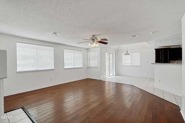 unfurnished living room featuring visible vents, wood-type flooring, a textured ceiling, and a ceiling fan