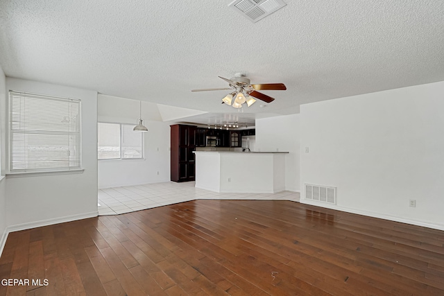 unfurnished living room with light wood finished floors, visible vents, a textured ceiling, and a ceiling fan