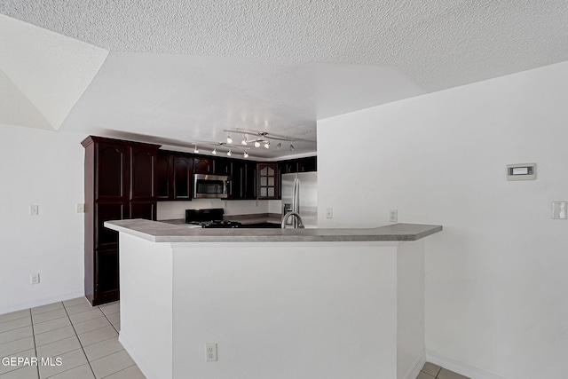 kitchen with light tile patterned floors, stainless steel appliances, a textured ceiling, and a peninsula