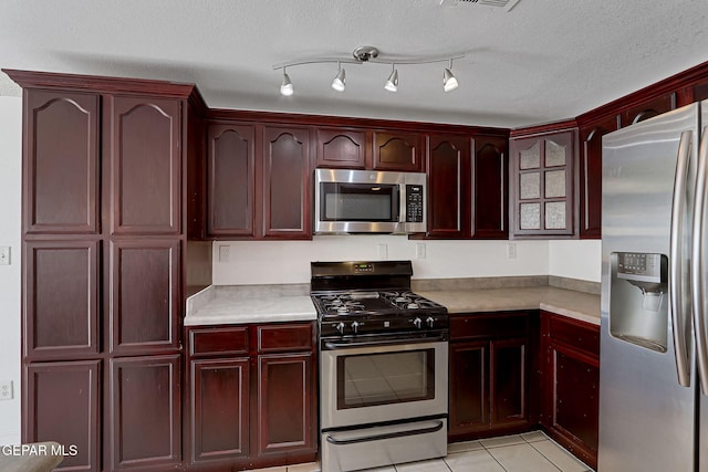 kitchen featuring a textured ceiling, stainless steel appliances, light countertops, light tile patterned floors, and dark brown cabinets