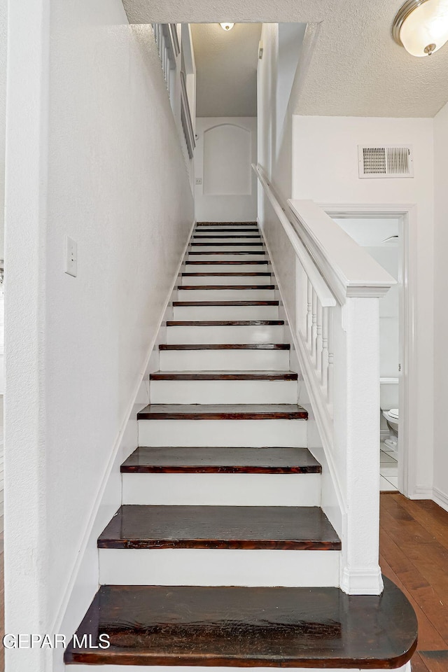 stairway with visible vents, a textured ceiling, baseboards, and hardwood / wood-style floors